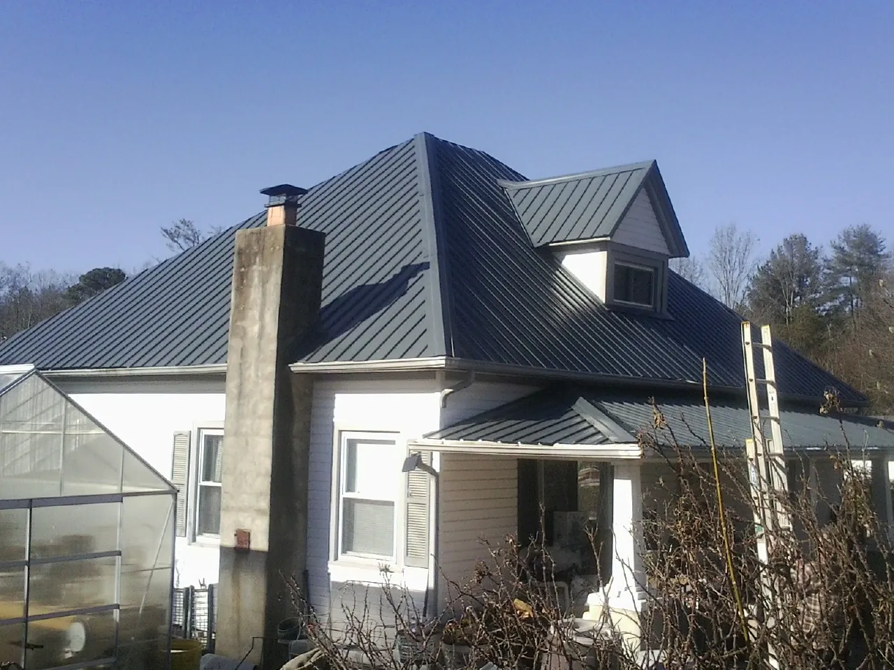 Dark blue standing seam metal roof on a white farmhouse with dormer — Slate & Tile Roof Repair by Roofing Brothers in Patriot