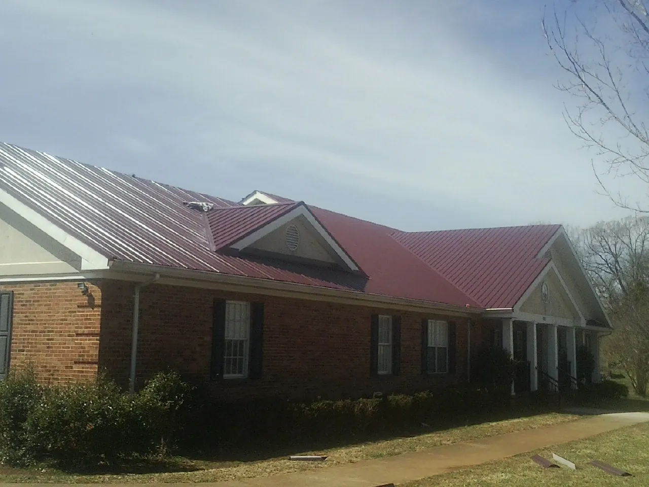 Red metal roof with gabled entries on a long brick building, from a Hail Damage Roof Repair job in Patriot