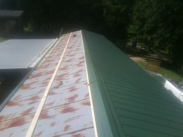 Old rusted panels beside newly installed green metal roofing — Wind Damage Roof Repair by Roofing Brothers in Patriot