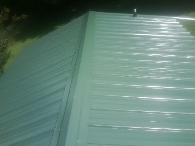 New green metal panels meeting at the ridge of a roof — Flat Roof Repair work by our crew in Patriot