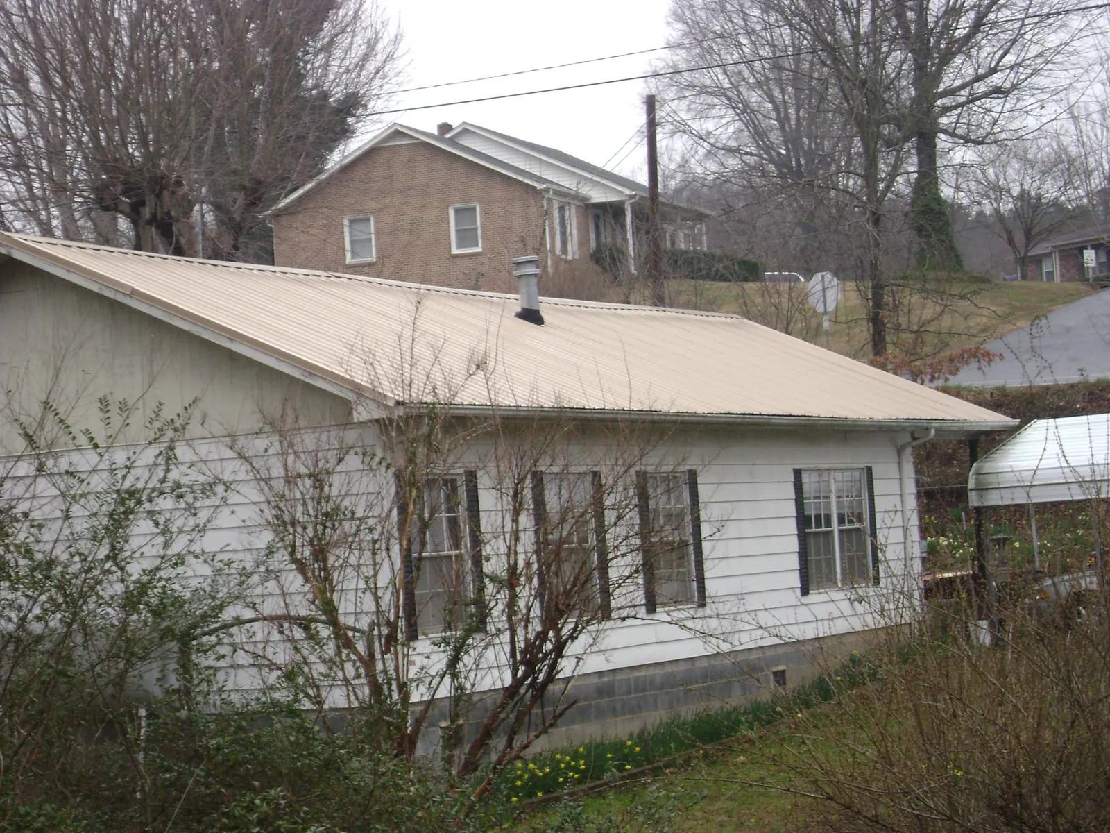 Tan metal roof on a white sided house set into a hillside — Commercial Roofing by Roofing Brothers in Patriot