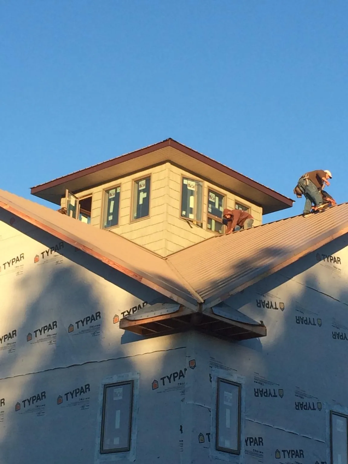 Roofers working around a rooftop cupola on a new metal roof at sunset in Patriot